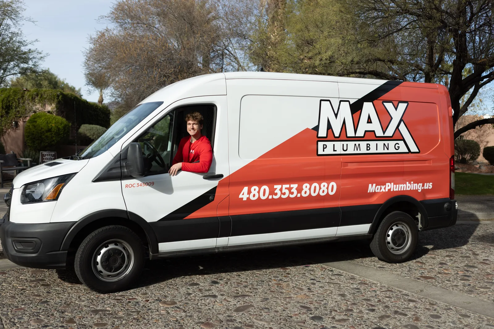 Chase, owner of Max Plumbing LLC, smiling from the driver window of the company van in Surprise, AZ