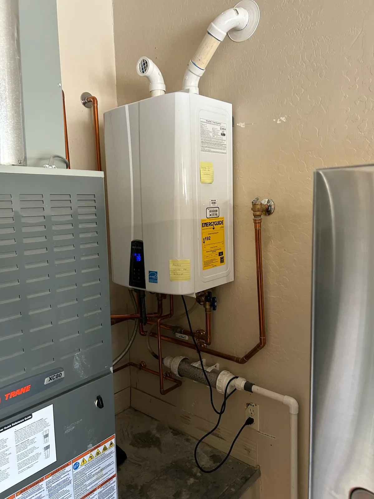 Wall-mounted tankless gas water heater with copper lines and PVC venting installed in a garage by Max Plumbing in Surprise, AZ